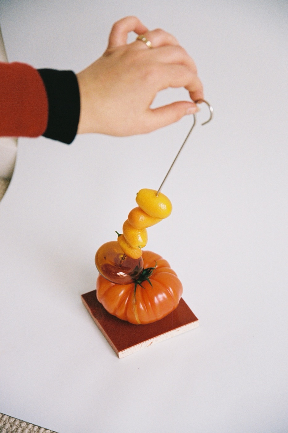 Hand holding a skewer of kumquats above a heirloom tomato