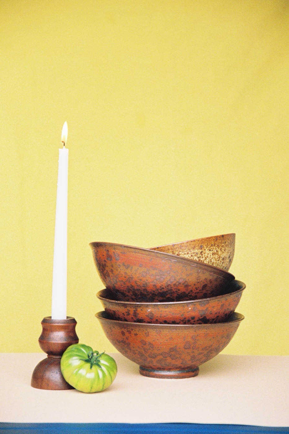 Lit candle beside stacked ceramic bowls and a green tomato